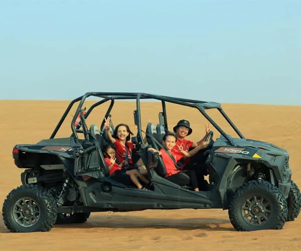 A happy family of four sitting in a large 4-seater black off-road dune buggy in the Dubai desert.